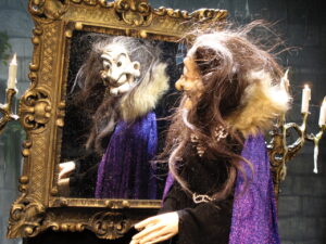 Die Hexe steht vorm Spiegel und bewundert sich selbst.