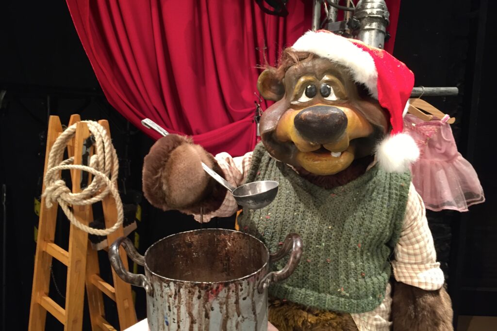 Bernie der Bär mit Weihnachtsmütze hält eine Kelle und trinkt vom Bärenpunsch